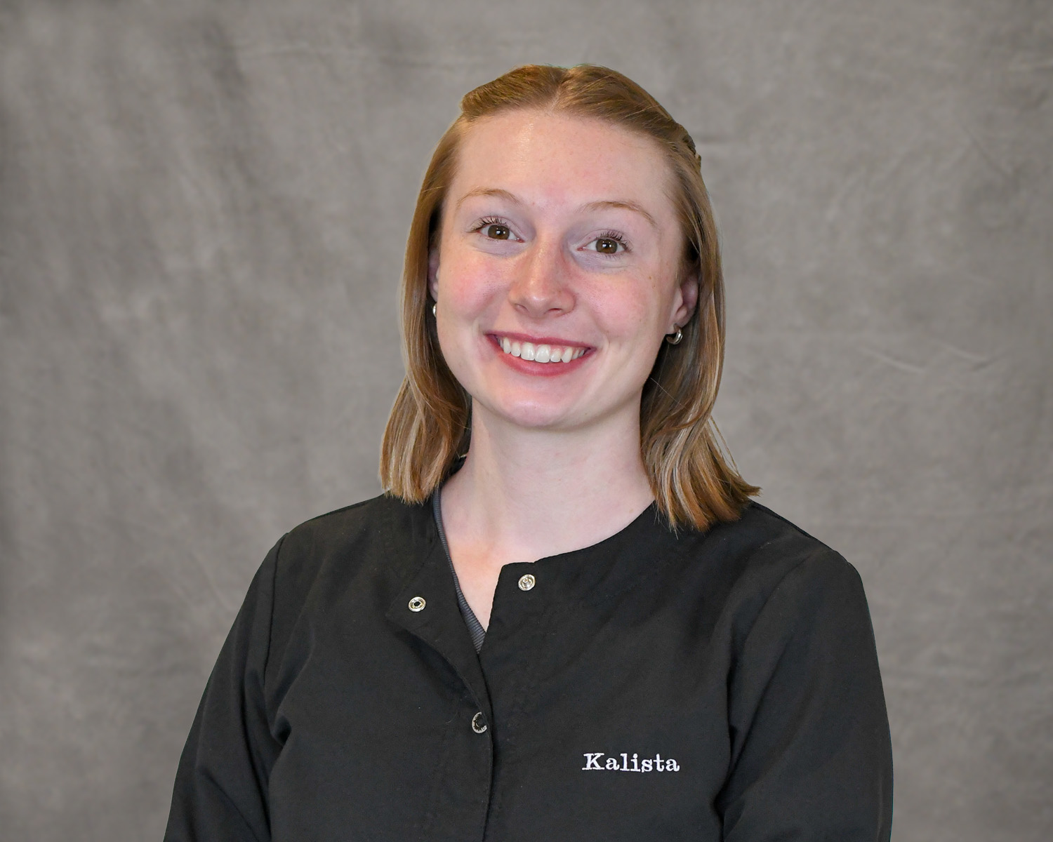 Kalista Sanchez, wearing a black scrub coat smiling for the camera.