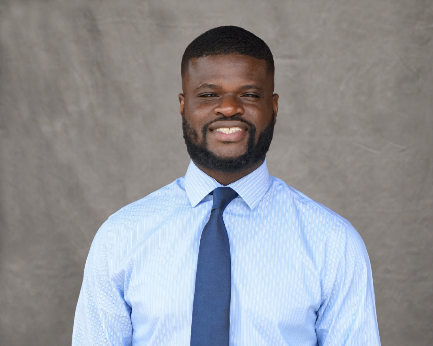 Dr. Amayke in a blue and white striped shirt and blue tie posing for a headshot.